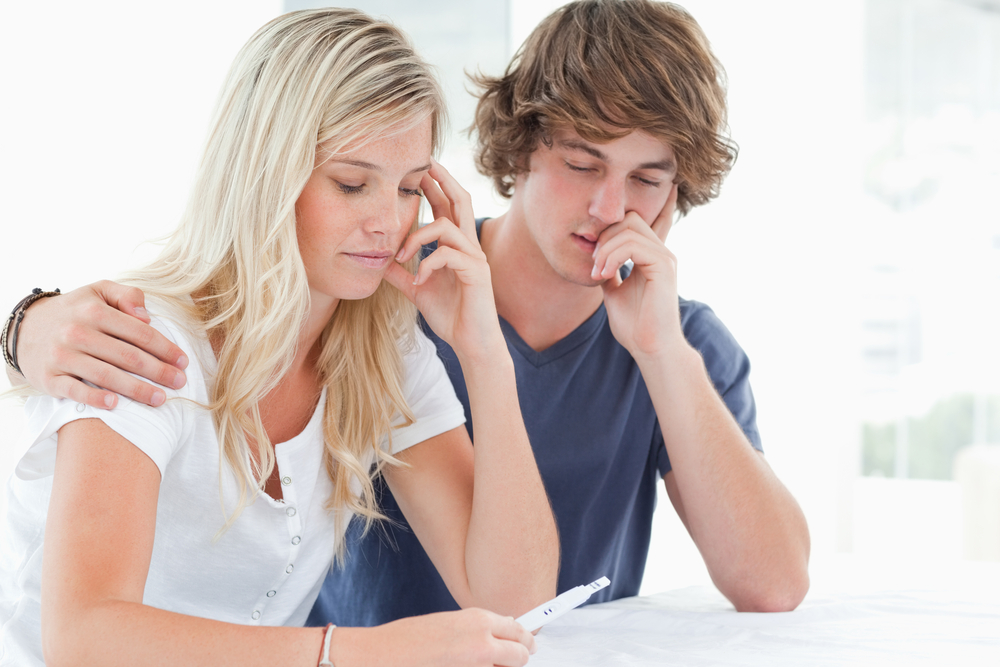 A worried couple hold each other as they look at a pregnancy test